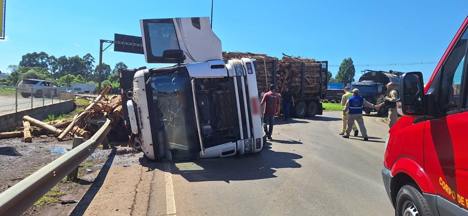 Caminhão carregado com toras tomba no trevo da Volvo