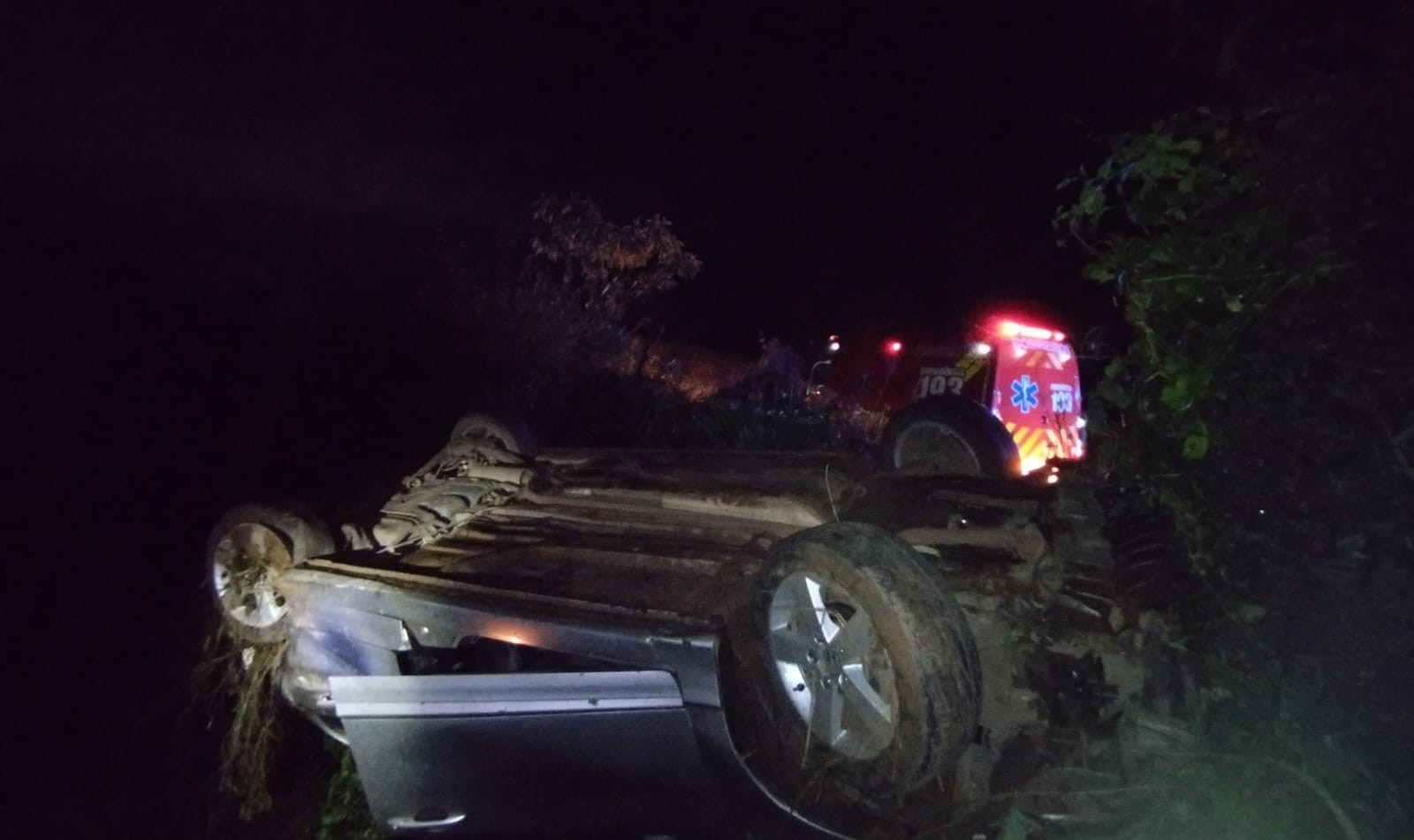 Mulher é socorrida por populares após sair da pista e capotar carro