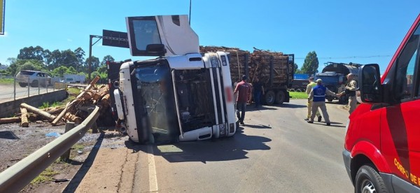 Caminhão carregado com toras tomba no trevo da Volvo