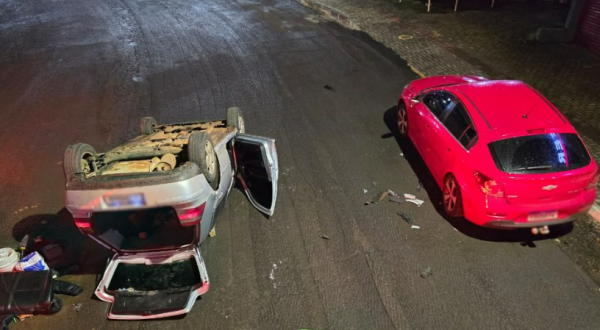 Carro bate em veículo estacionado e capota em avenida de SC